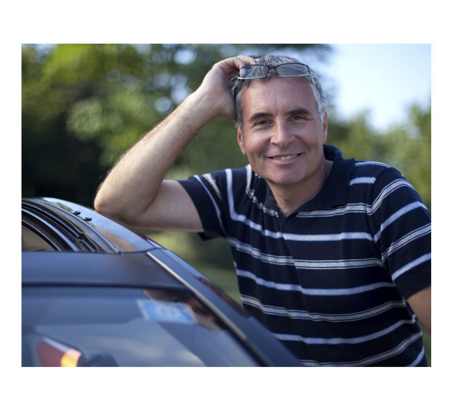 middle aged man standing next to his car on a sunny day