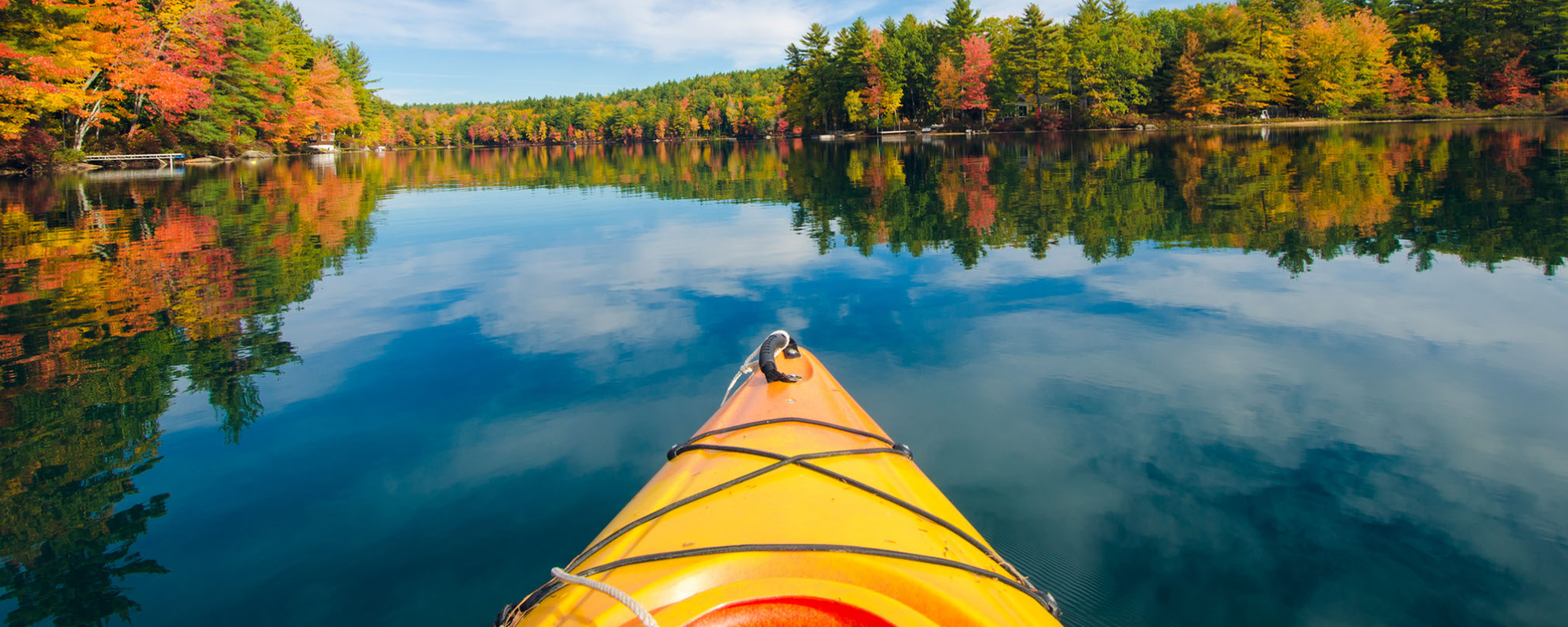 the front of a kayak on a lake with a beautiful fall view
