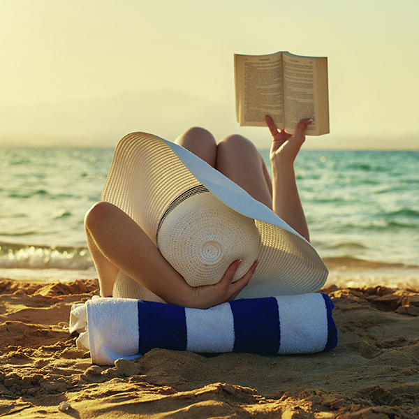 woman lying on beach and reading, sunset time, at the edge of sea, sunhat.photo taken in summer day outdoors.