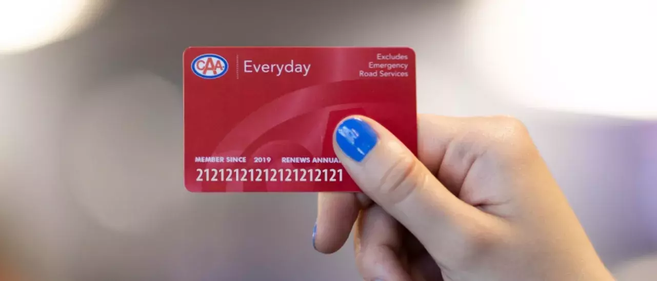 hand with blue nailpolish holding a red CAA membership card with the word Everyday at the top left to the right of the CAA logo. Top right of the card says Excludes Emergency Road Services hand with blue nailpolish holding a red CAA membership card with the word Everyday at the top left to the right of the CAA logo. Top right of the card says Excludes Emergency Road Services