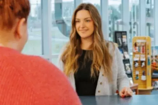female with long brown hair wearing a grey cardigan being asissted by a representative at a counter female with long brown hair wearing a grey cardigan being asissted by a representative at a counter